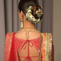 A classic bridal bun decorated with a ring of fresh white flowers and a traditional jadau pin. This hairstyle is timeless, elegant, and perfectly complements a royal bridal look.