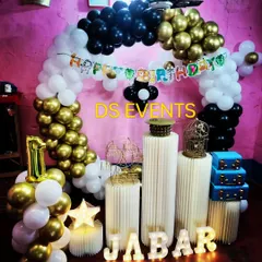 This elegant black, white, and gold theme is a stylish option for a first birthday party. The decor features a circular balloon arch, light-up marquee letters for the name, and modern ribbed plinths for the cake display.