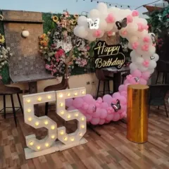 An elegant 55th birthday celebration on a terrace. I used a pink and white balloon arch, a "Happy Birthday" sign, and large marquee numbers to create a beautiful photo corner.