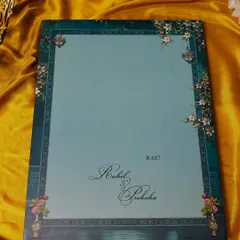 A clean and elegant invitation cover in a soft teal, with the couple's names in a beautiful script, framed by a traditional border.