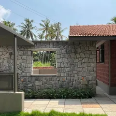 A wall of random rubble masonry provides a rugged, textural contrast to the smooth, finished surfaces of this Mangalore holiday home. The window opening is left without a frame to emphasize the thickness of the stone wall.