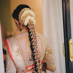 A back view of a classic South Indian bridal hairstyle. The neat bun is adorned with jasmine flowers, leading into a long braid decorated with traditional gold ornaments.