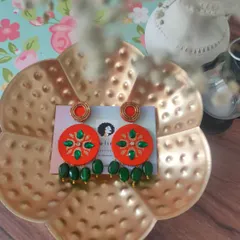 A vibrant pair of hand-painted earrings in orange and green. I used zardozi techniques to create the floral pattern, and the green bead drops add a beautiful finishing touch.