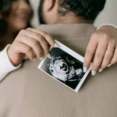 A creative and sweet announcement. The sonogram is held up against the father-to-be's back, with the mother's happy face blurred in the background, symbolizing the new life that connects them.