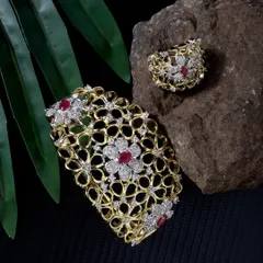 A stunning floral-design bracelet and ring set with ruby and diamond details. The lighting is carefully controlled to capture the sparkle of the stones against a natural, textured background.