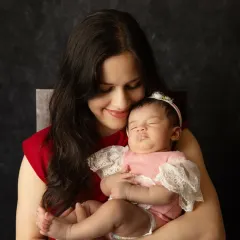 A mother gazes lovingly at her peacefully sleeping newborn, cradled securely in her arms during their first photoshoot together.