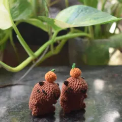 Two of my crochet capybara desk buddies, each balancing a tiny orange on its head. It's a quirky and adorable detail that makes these little guys a customer favorite.