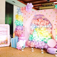 This stunning photo booth for a Candyland party features a wall of pastel balloons creating a rainbow effect inside a pink arch. Oversized candy props like macarons and lollipops complete the delicious scene.