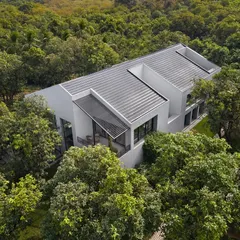 The clean, white monolithic form of the house contrasts with the organic texture of the surrounding trees. The roofline is punctuated by openings for the open-to-sky courtyards that bring light into the home's core.