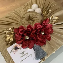 A festive gift wrap for a wedding anniversary. The golden fabric is complemented by rich red flowers, a grey tassel, and a custom "Happy Wedding Anniversary" card.