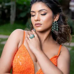 For a pop of color, this emerald green ring and matching tiered earrings are a perfect choice. They add a luxurious and vibrant touch to this orange gown.