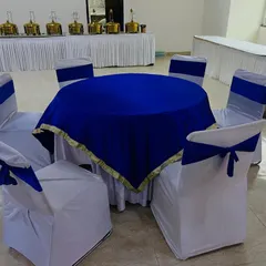 An elegant guest seating arrangement with a round table covered in royal blue velvet and chairs with matching sashes.