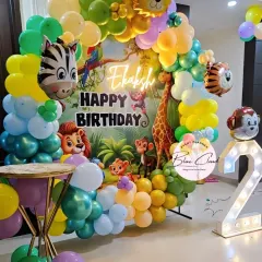 A lively jungle-themed birthday party with a circular balloon backdrop and character cutouts. The decor includes a neon 'Happy Birthday' sign and an illuminated number '2'.