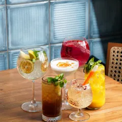 A vibrant collection of five different cocktails and coolers, expertly styled on a wooden table. This image is perfect for a bar or restaurant menu, showcasing the colorful and diverse drink offerings.