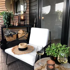 We designed this chic and modern balcony corner for relaxation. The space features a comfortable armchair with white cushions, black slatted wall paneling, and natural elements like woven baskets and potted plants, creating a perfect spot to unwind.
