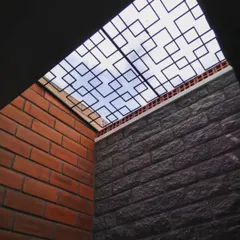 A geometric grill under a skylight frames the sky, turning it into a piece of art. This feature allows light to pour into the core of the building while adding a decorative element that interacts with the stone and brick walls.
