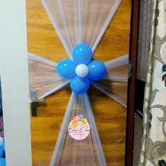 A simple and elegant door decoration using white netting and a blue balloon flower to welcome guests.