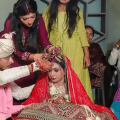 The groom applies sindoor to the bride's forehead, with family members assisting in the ritual. This photo captures the communal and familial nature of Indian weddings, showing the involvement of loved ones in the sacred ceremony.