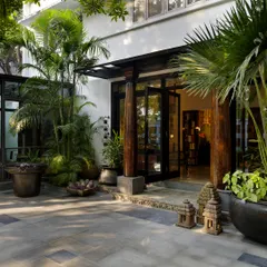 The entrance porch of the Courtyard Home, featuring old teakwood columns from Kerala and lush tropical plants. This space sets a welcoming and organic tone, blending architectural elements with nature.