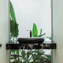 A hint of nature makes everything better. This powder room features a minimalist black sink on a marble counter, with a window looking directly into a private green space, bringing the garden inside.