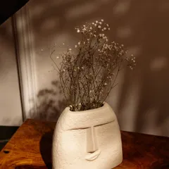 The same face-shaped vase, now with dried baby's breath flowers. This simple addition transforms the product and shows its versatility.
