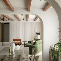 A look from the dining area into the living room of the Parisian home. The archway perfectly frames the scene, highlighting the layers of texture from the fluted wall, the plush green sofa, and the warm wooden ceiling beams.
