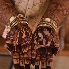 A close-up of the rich henna stain on a personalized couple portrait design. One palm shows a silhouette of the couple expecting, while the other features a detailed portrait of them together.