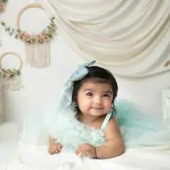 A beautiful, serene portrait of an infant lying on a soft white blanket. Her gentle smile and the dreamy mint green dress create a peaceful image.