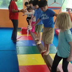 Walking the balance beam is a great way to develop focus and coordination. Here, a line of children carefully makes their way across with a coach's guidance.