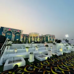 This wide-angle shot captures the full scale of the palatial wedding stage against the evening sky. The combination of the intricate backdrop, the expansive custom carpet, and the tiered floral arrangements creates a truly magnificent setting.