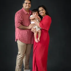 A classic family-of-three portrait against a dark backdrop. This timeless style is perfect for celebrating a milestone like a first birthday.