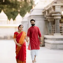 A full-length shot of a couple walking hand-in-hand through the temple grounds, capturing the grace of the expecting mother in her beautiful red and gold saree.
