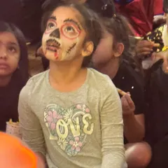 This spooky-cute skeleton face paint is a perfect example of the amazing work our artists do. Look at her expression, completely captivated by the show.