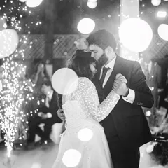 An intimate black and white photo of the couple's first dance. The use of lens flare and the surrounding sparklers creates a dreamy, romantic atmosphere, focusing entirely on their close embrace.