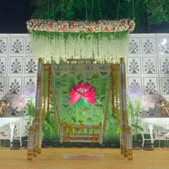 This is a complete stage setup for a traditional naming ceremony. The design centers around the beautifully decorated palna, framed by a fresh green backdrop, hanging florals, and soft lighting to create a peaceful and celebratory atmosphere.