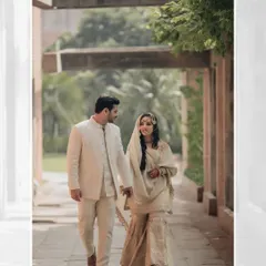 The couple walks hand-in-hand through a sunlit corridor, their smiles and gentle hold capturing a moment of pure, serene love.