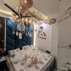 I specialize in creating personal and romantic birthday surprises right in your bedroom. This setup features elegant rose gold and white balloons on the ceiling, more balloons scattered on the bed, and a special wall display with your personal photos hanging from ribbons.