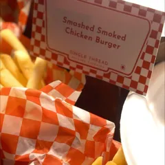 A close-up of the "Smashed Smoked Chicken Burger" sign, nestled in a classic red-and-white checkered paper basket of fries. This detail shot highlights one of our specific, delicious burger offerings.