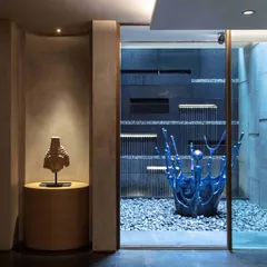In the basement courtyard, a serene water feature is anchored by a vibrant blue sculpture by Alex Davis. The installation creates a tranquil focal point, blending the elements of water, stone, and contemporary art.