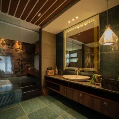 A bathroom that balances rustic and modern elements. It features green stone floor tiles, a floating wooden vanity, and a slatted wood ceiling, with a dramatic stone accent wall in the shower area creating a focal point.