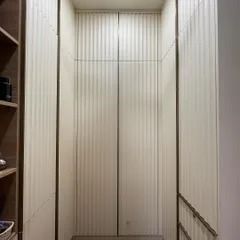 A direct view into the walk-in closet, showcasing the beautiful texture created by the vertical fluted panels. The off-white color keeps the space feeling bright and airy.