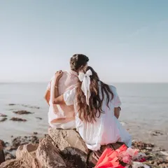 A quiet moment together, watching the sun set over the ocean. This pre-wedding shot captures the romance and anticipation before the big day, with a beautiful bouquet adding a pop of color to the serene seascape.