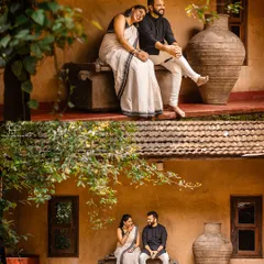 A candid, romantic moment captured at a traditional heritage home. The bride, in a classic white and black saree, rests her head on her partner's shoulder, showcasing a quiet, intimate connection in a nostalgic setting.