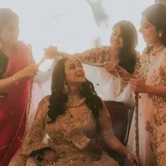 A bride shares a laugh with her bridesmaids as they help her get ready. The beautiful golden light in the room adds to the warmth of this candid moment of friendship.