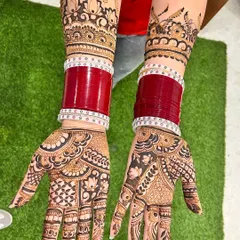 This full coverage bridal henna is designed to complement the traditional red chooda bangles. The pattern features intricate floral work on the palms and a beautiful crown-like design on the wrists.