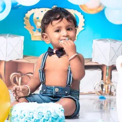 A little prince celebrating his first birthday with a royal blue cake smash. The setup includes a crown, balloons, and a delicious-looking cake ready to be smashed.