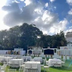 A wide view of the outdoor venue during setup, showing the clean, all-white table arrangements and the catering stations in the background.