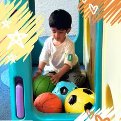 A young boy explores different types of balls in a playhouse. This unstructured play allows for imaginative exploration and the development of motor skills.