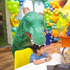 A friendly T-Rex mascot surprises a guest during a dinosaur-themed birthday party. My themed decorations and entertainment create an immersive and exciting atmosphere for everyone.