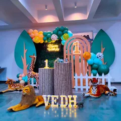 A wild jungle theme for Vedh's first birthday. The setup includes realistic animal props like a lion, tiger, and giraffe, set against a backdrop of lush greenery and wooden textures to create an exciting safari vibe.